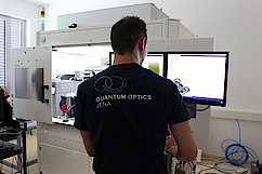 Mann in schwarzem T-Shirt steht dem Betrachter mit Rücken zugewendet, im Hintergund Monitor und große Maschine