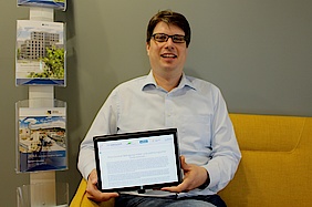 Markus Henkenmeier, Prokurist bei JenaWirtschaft, sitzt auf einem Sofar und präsentiert die Unternehmensbefragung auf einem Tablett.