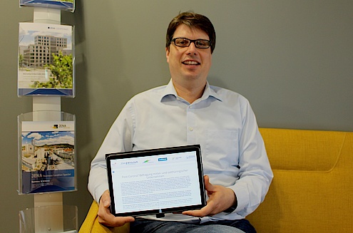 Markus Henkenmeier, Prokurist bei JenaWirtschaft, sitzt auf einem Sofar und präsentiert die Unternehmensbefragung auf einem Tablett.
