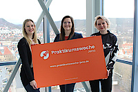 3 Frauen stehen nebeneinander und halten großes oranges Schild 