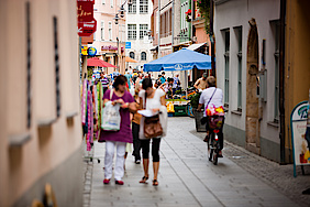 Blick in Einkaufsstraße mit vielen Menschen in der Mitte und Läden links und rechts, unscharf fotografiert