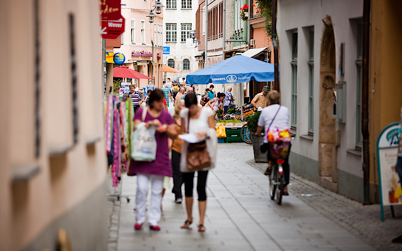 Blick in Einkaufsstraße mit vielen Menschen in der Mitte und Läden links und rechts, unscharf fotografiert