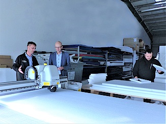 Zwei Männer in stehen an einer Produktionsmaschine für Verpackungsmaterial. 
